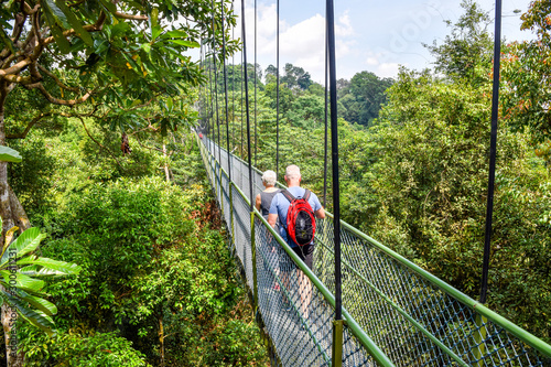 Photo Hikers Walking Across a Pedestrian Walking Bridge in Southeast Asian Jungle / Na