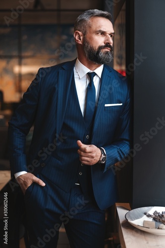 Tablou canvas Stylish bearded man in a suit standing in modern office