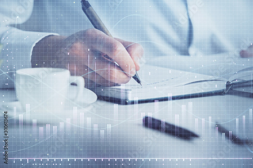 Double exposure of man's hands writing notes of stock market with forex chart.