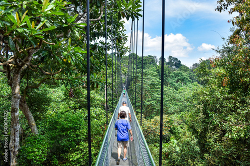 Photography Hikers Walking Across a Pedestrian Walking Bridge in Southeast Asian Jungle / Na