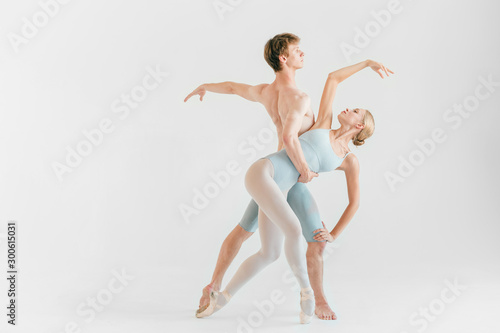 Young couple of modern ballet dancers posing over white studio background