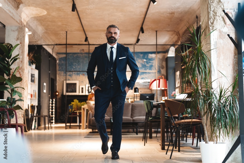 Stylish bearded man in a suit standing in modern office Stylish bearded man in a suit standing in modern office