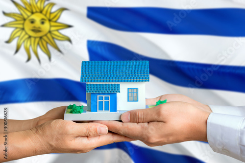 Uruguay real estate concept. Man and woman holding miniature house in hands. Citizenship theme and national flag on background.