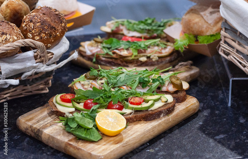 Sandwiches with tomatoes, lettuce, ham, lemon and arugula on dark bread. On wooden background