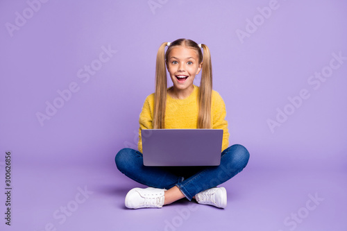 Full size photo of amazed child sit folded crossed legs work computer get social media notification scream wow omg wear yellow pullover sneakers isolated over purple color background