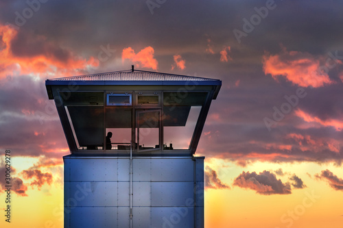 An air traffic control tower with the silhouette of an unidentifiable male traffic controller standing, cloudy weather, Iceland.