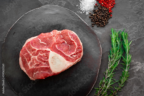 Raw beef meat osso buco steak on round slate cutting board. Top view photo