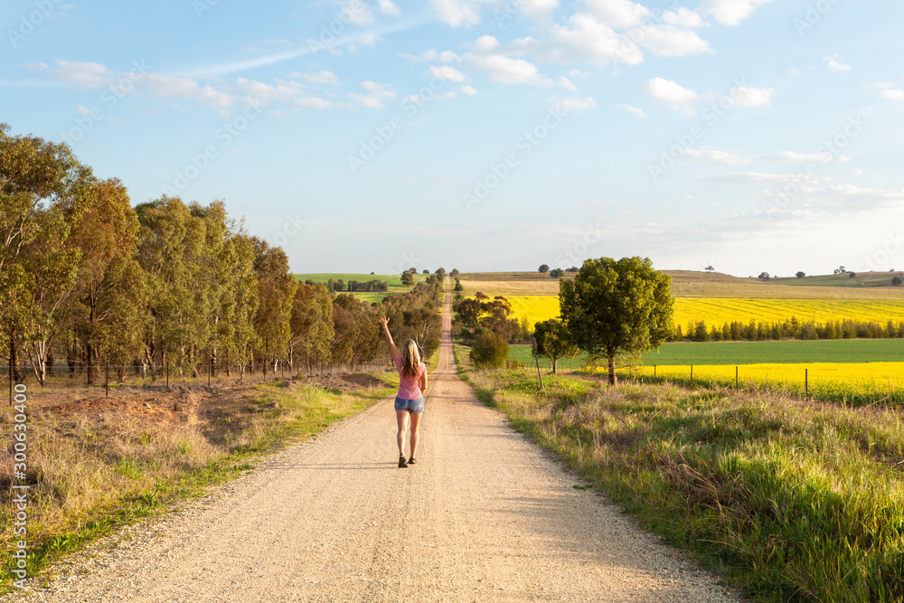 Fototapeta premium Woman walking along a dusty road among the rural fields