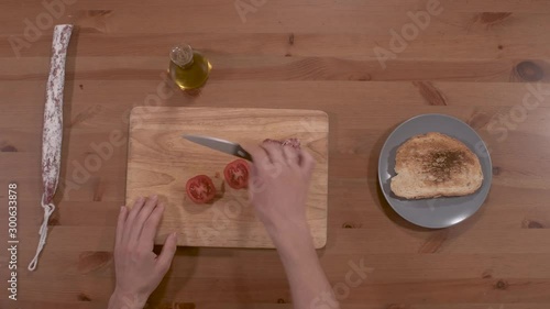 smearing bread with tomato, typical Catalan food, for breakfast, snack, dinner, accompanied by olive oil, and sausage, totally top view, only the hands are seen with a wooden bottom photo