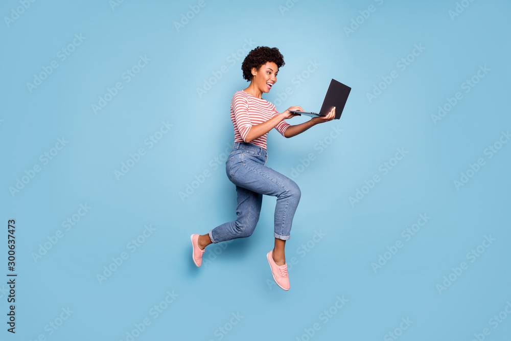 Full length body size side profile photo of pretty cheerful cute nice charming youngster typing before laptop wearing jeans denim striped shirt isolated pastel color blue background - obrazy, fototapety, plakaty 