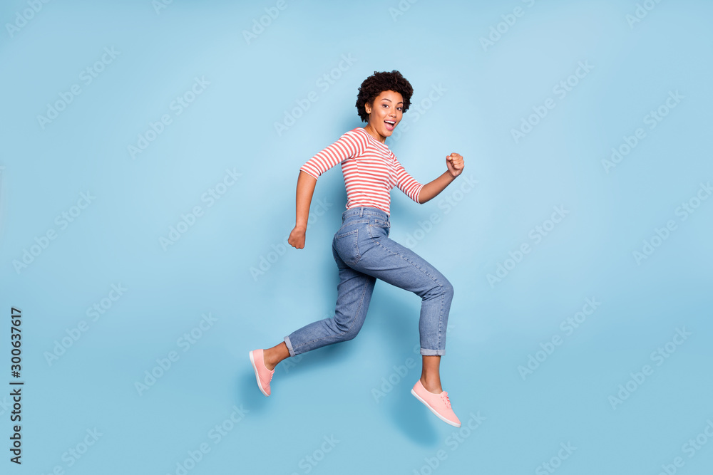 Side profile full length body size photo of pretty sweet cheerful girlfriend wearing jeans denim striped shirt epxressing funny emotions jumping running isolated pastel blue color background