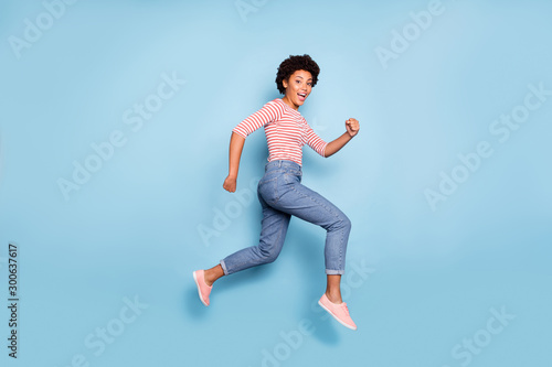 Side profile full length body size photo of pretty sweet cheerful girlfriend wearing jeans denim striped shirt epxressing funny emotions jumping running isolated pastel blue color background © deagreez