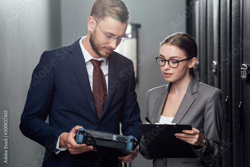 handsome businessman holding reflectometer near businesswoman in data center photo