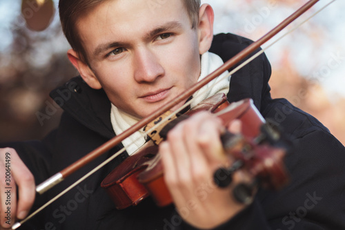 face of a young elegant man playing the violin on autumn nature backgroung, a boy with a bowed instrument practicing, musical performance outdoors, concept of hobby and art