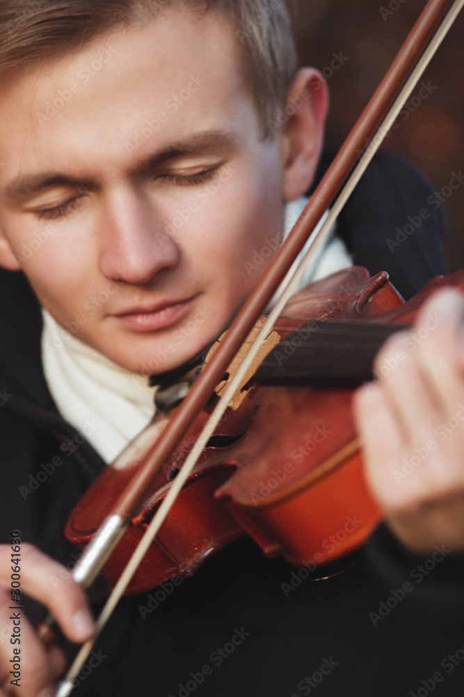 close-up portrait of a young elegant man playing the violin on autumn nature backgroung, boy's face with musical instrument under his chin, concept of hobby, art and lifestyle close-up portrait of a young elegant man playing the violin on autumn nature backgroung, boy's face with musical instrument under his chin, concept of hobby, art and lifestyle