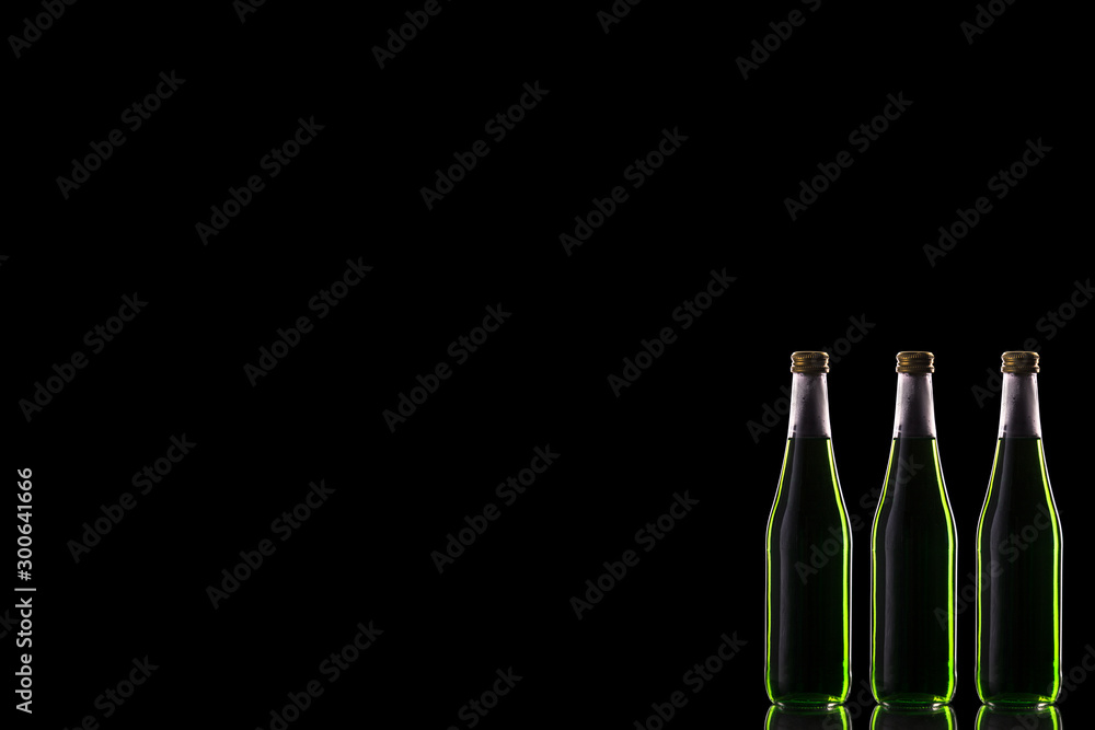 Three small glass bottles with a green drink stand on a mirror surface against a dark background with the right.