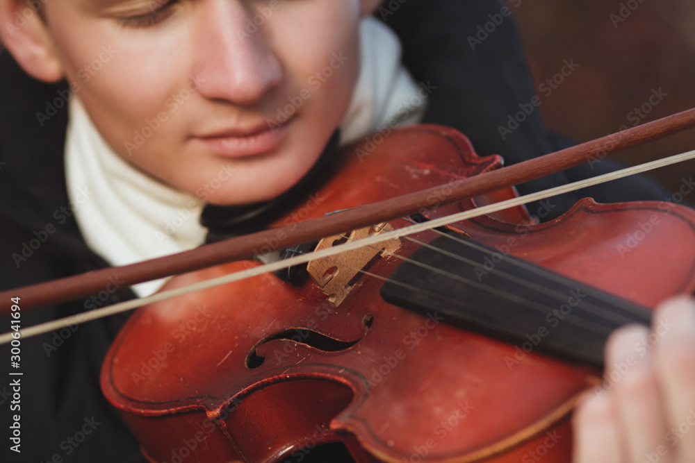 close-up portrait of a young elegant man playing the violin on autumn nature backgroung, boy's face with musical instrument under his chin, concept of hobby, art and lifestyle close-up portrait of a young elegant man playing the violin on autumn nature backgroung, boy's face with musical instrument under his chin, concept of hobby, art and lifestyle