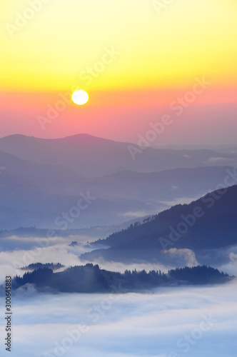 Fantastic view of the mountain peaks in the fog and the rising sun over the mountains. Top view from the top of the mountains.
