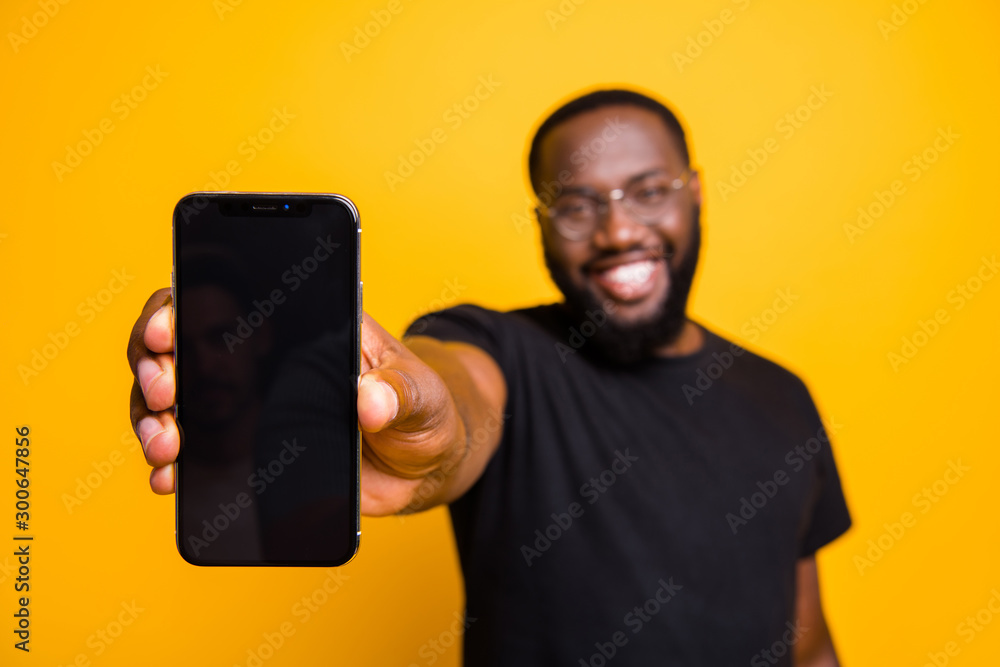 Portrait of positive afro american guy hold smartphone show modern technology gadget advertise promotion wear casual style outfit isolated over yellow color background - obrazy, fototapety, plakaty 