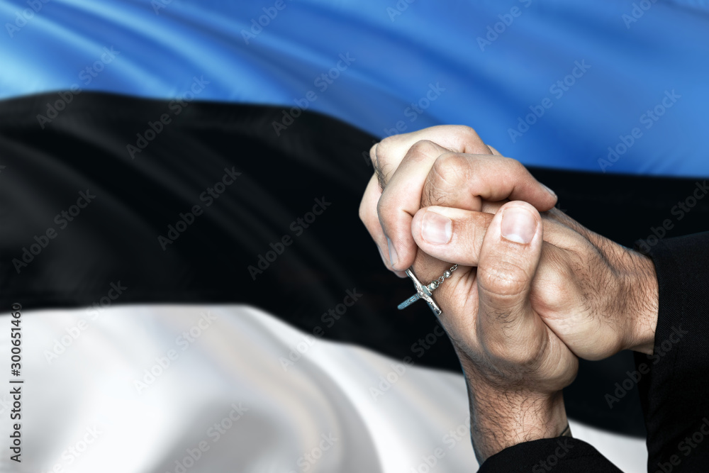 Estonia flag and praying patriot man with crossed hands. Holding cross, hoping and wishing.