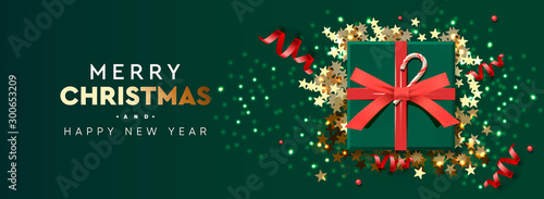 Holiday background Merry Christmas and Happy New Year. Xmas design with realistic festive objects, sparkling lights garland, green gift box, glitter gold confetti, red streamers. Horizontal banner