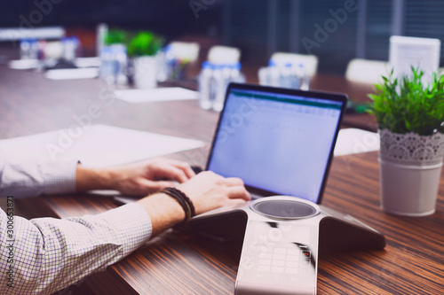 Male hand,  IP phone and laptop on the office table. Ip telephony and video meetings for business concept. Close up.