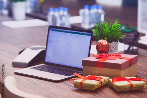 Young businessman surrounded by gifts in office. Workplace, cup of tea, laptop, ip phone and boxes. Christmas gift from colleague. Secret Santa office tradition. New year background.
