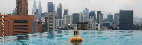 Young happy girl swimming alone in the infinity pool on rooftop in Kuala Lumpur in Malaysia. Horizontal photo.