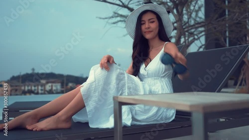 Enjoy woman sitting near swimming pool with long dress, sunglasses,hat resting on summer at resort, Travel women relaxation people lifestyle UHD 4k cinematic footage