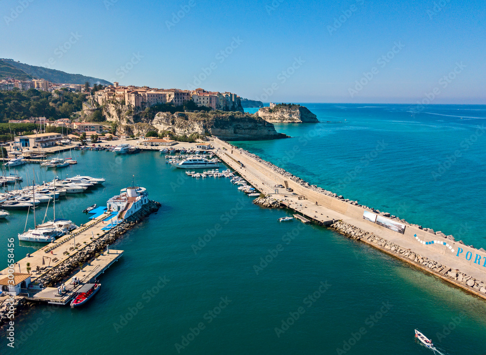 Aerial view of boats moored at the Port of Tropea, Calabria, Italy. Houses overlooking the sea. Beach and Sanctuary on the horizon. Italian coasts