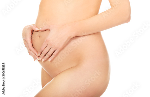 Nude pregnant woman in eight month touching belly with hands. Maternity concept.