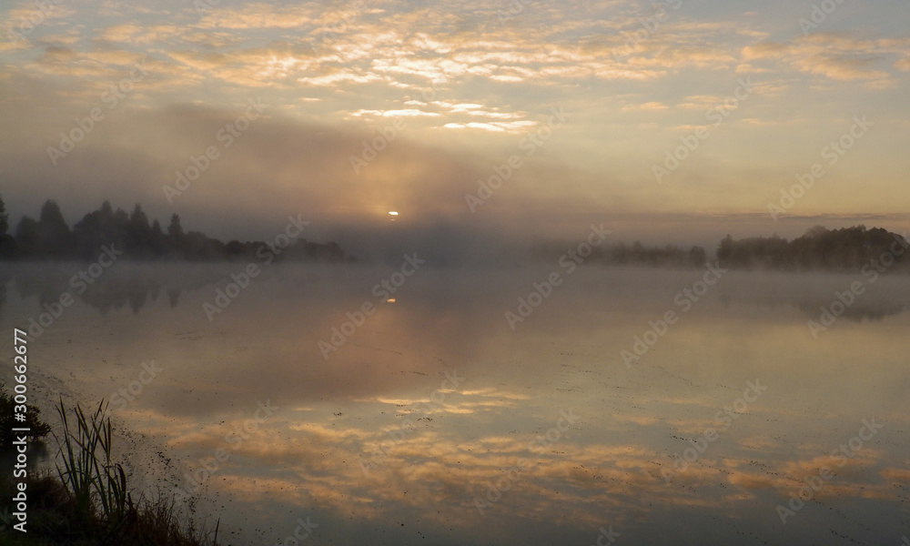 Beautiful, colorful landscape of a foggy lake during sunrise. Misty dawn in the lake. Bright sun over lake. Beautiful, colorful landscape of a foggy lake during sunrise. Misty dawn in the lake. Bright sun over lake.