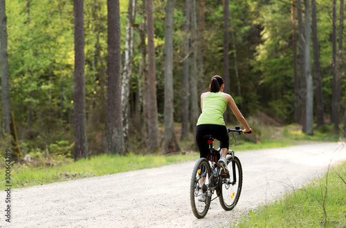 Back view of woman riding bike on path in forest. She exploring with joy.