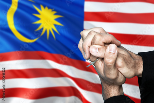 Malaysia flag and praying patriot man with crossed hands. Holding cross, hoping and wishing.