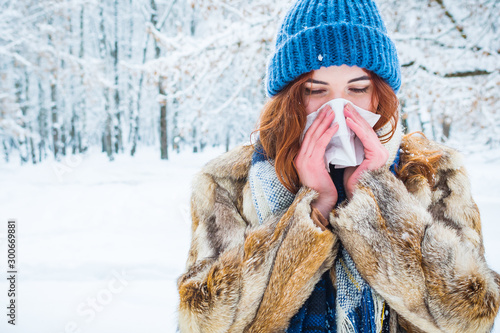 portrait of a young woman in the winter forest. a beautiful girl sneezes into a napkin. get sick in winter.