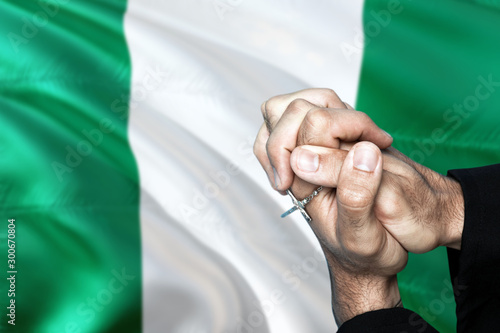 Nigeria flag and praying patriot man with crossed hands. Holding cross, hoping and wishing.