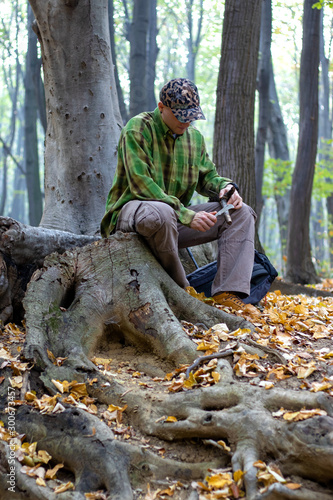 Man with knife sharpening a wooden stick for campfire in the forest. Bushcraft, hunting and people concept. - Image
