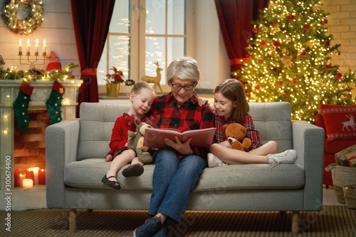 Photo Grandmother reading  to granddaughters near Christmas tree.