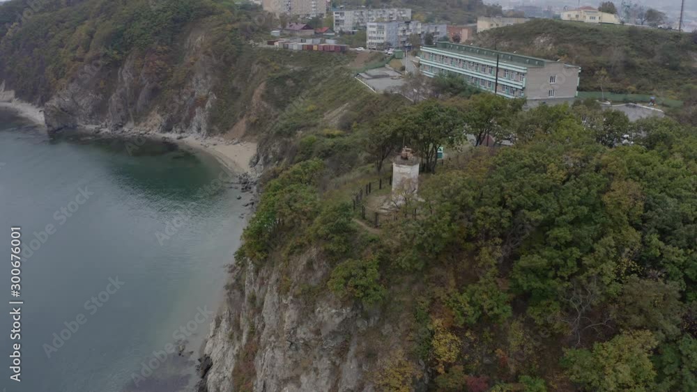 Aerial pivot shot of an old
white lighthouse beacon, standing on top of a cliff, surrounded by green trees, on a cloudy overcast day. Aerial pivot shot of an old
white lighthouse beacon, standing on top of a cliff, surrounded by green trees, on a cloudy overcast day.