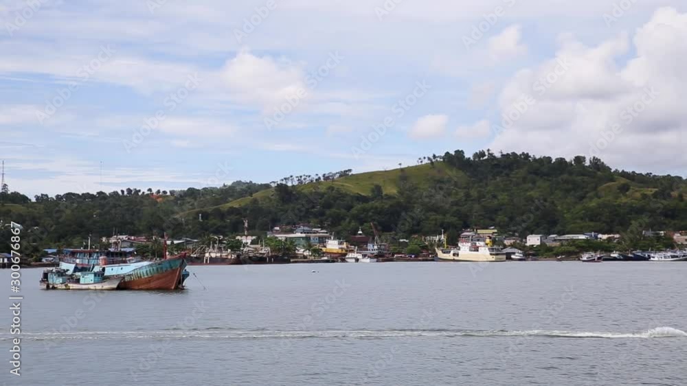 Small boat drives past a coast with many old houses - RAJA AMPAT, INDONESIA Small boat drives past a coast with many old houses - RAJA AMPAT, INDONESIA
