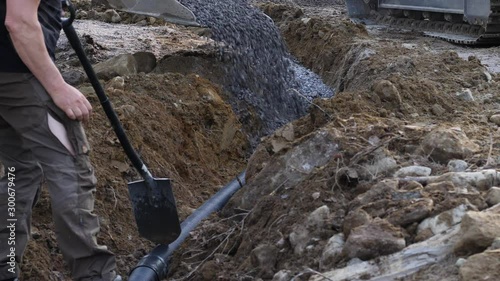 Static shot of a man looking at a machine pouring gravel on a pipe, making drainage, for his future house, in Ostrobothnia, Finland photo