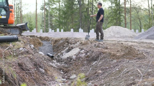 Static shot of a man looking at a machine, digging a drainage, for a house, in Ostrobothnia, Finland photo