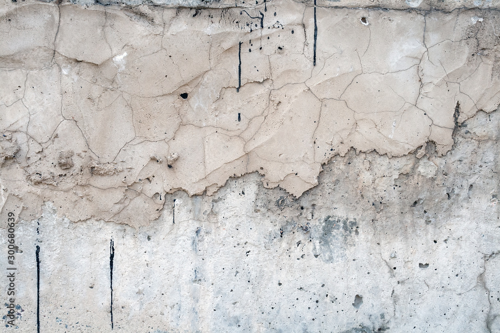 Obraz premium Gray wall covered with an uneven rough layer of plaster with holes, irregularities, cracks and thin traces of flowing black resin
