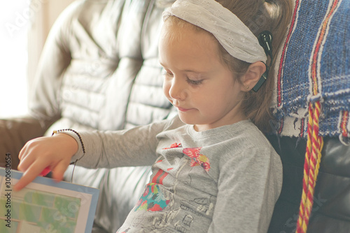 Blonde little girl with cochlear implant reading a book at home. Hear impairment and deaf community concept with empty copy space for Editor's text. photo