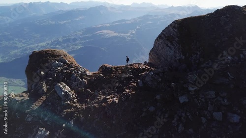 Drone shot following a hiker backpacking along a trail near the edge of the peak of Mountain Brisi, one of the Churfirsten Mountains in Switzerland.  photo