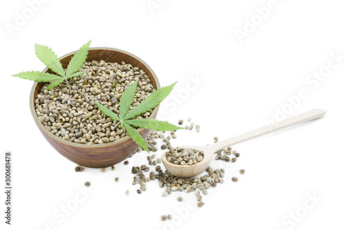 Cannabis Hemp seeds in a wooden bowl and spoon and green leaves isolated on white background