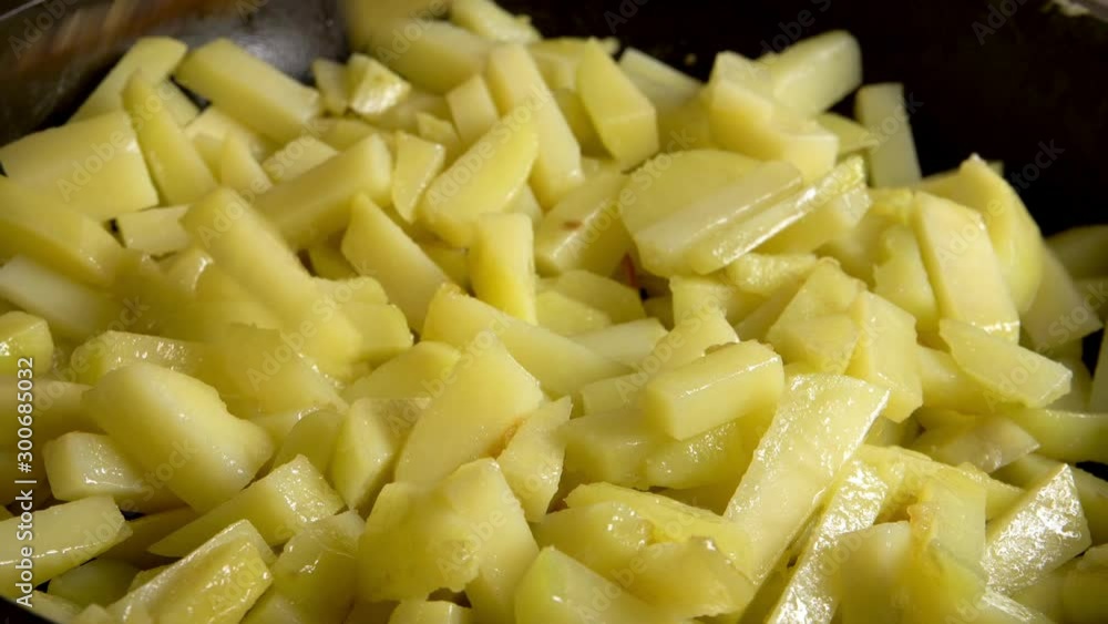 stirring potato slices in a pan with a wooden kitchen spatula while frying close-up stirring potato slices in a pan with a wooden kitchen spatula while frying close-up
