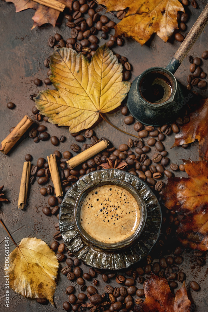 Black coffee espresso with foam in black ceramic cup, with saucer, cezve coffee pot, autumn leaves, spices and roasted beans above over brown texture background. Flat lay - obrazy, fototapety, plakaty 