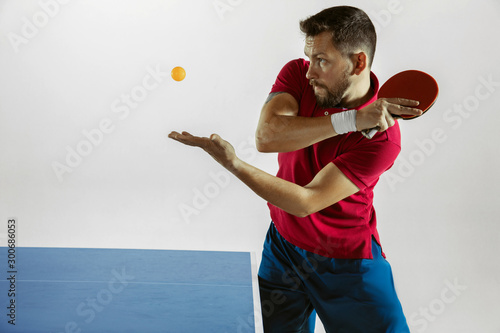 Young man plays table tennis on white studio background. Model in sportwear plays ping pong. Concept of leisure activity, sport, human emotions in gameplay, healthy lifestyle, motion, action, movement photo