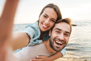 Image of man giving piggyback ride woman and taking selfie photo